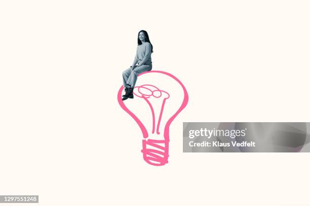 smiling woman sitting on large pink light bulb - innovation white background stock pictures, royalty-free photos & images