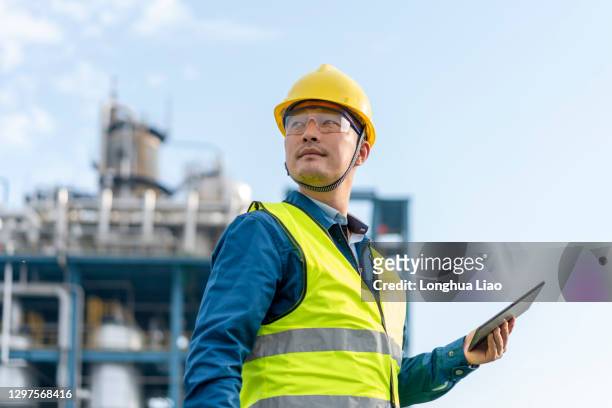 a young engineer uses a tablet computer outside a chemical plant - oil and gas workers stock-fotos und bilder