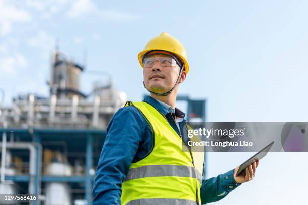 a young engineer uses a tablet computer outside a chemical plant - oil and gas industry stock pictures, royalty-free photos & images