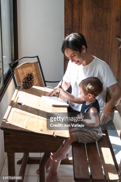 vertical photo of a child who is drawing with his mother smiling in a notebook on an antique wooden desk. the mother hugs him with one arm. - portrait of school children and female teacher in field stock pictures, royalty-free photos & images