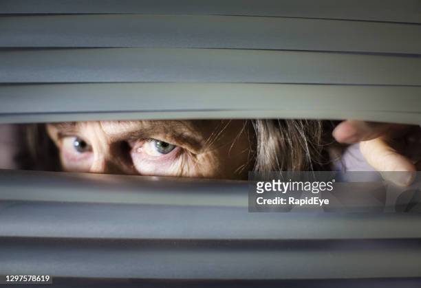 mujer mayor mirando ansiosamente a través de persianas - entrometido fotografías e imágenes de stock