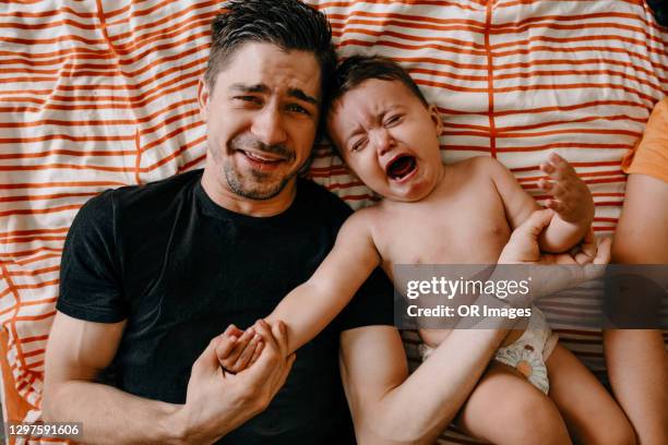 father and crying son lying in bed - hombre llorando fotografías e imágenes de stock