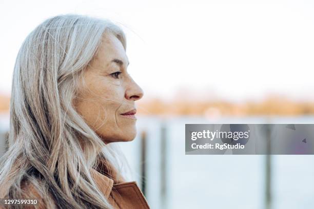 headshot van een nadenkende rijpe vrouw die de afstand bekijkt - mature woman winter stockfoto's en -beelden