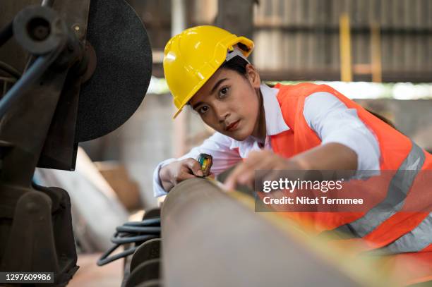 asian female industrial worker using tape measure measuring the length of the steel pipe in factory warehouse. - measure length stock pictures, royalty-free photos & images
