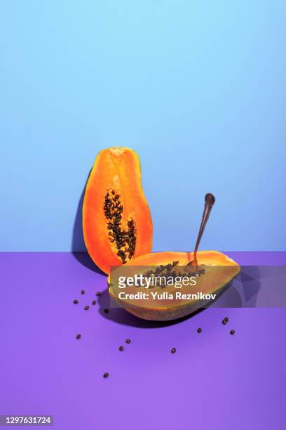 papaya with spoon on the purple-blue background - halved stock-fotos und bilder