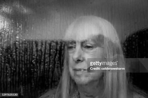 depressed senior woman looking out of rainy window - violence prevention stock pictures, royalty-free photos & images