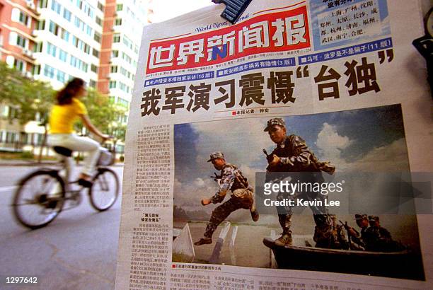 Chinese cyclist rides by a newspaper with a front page photo featuring the People's Liberation Army soldiers in military exercise with the headline...