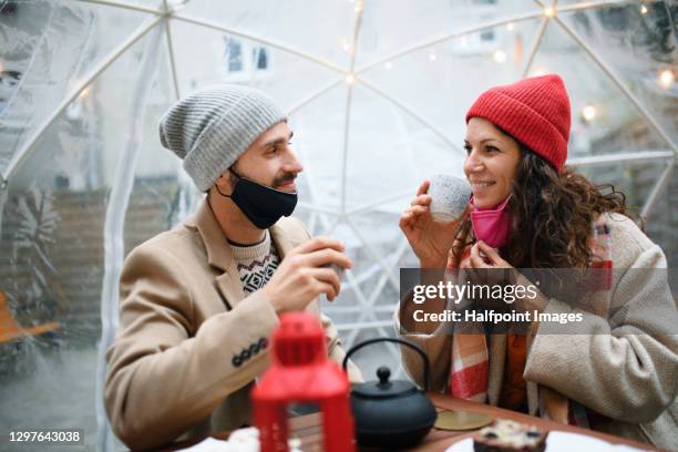 couple with face mask dining in plastic igloo dome tent outside cafe. - coronavirus dating stock pictures, royalty-free photos & images