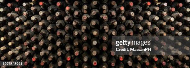 horizontal pannel showing many old wine bottles stored in a cellar for aging. - composizione stock pictures, royalty-free photos & images