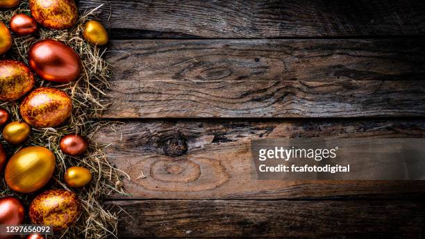 het nest van het stro met gouden en brons gekleurde paaseieren op rustieke houten lijst. ruimte kopiëren - rustic wood stockfoto's en -beelden