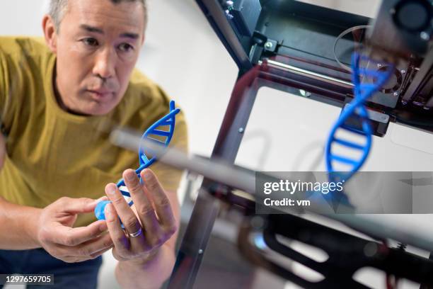 mixed-race man holding dna structure chain model and comparing it to one that is being printed - 3d printer product stock pictures, royalty-free photos & images