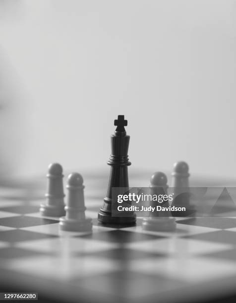 black king surrounded by white pawns on chess board - circondare foto e immagini stock