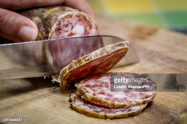 artisanal friulian salami being sliced on a rustic wooden cutting board - salami stock pictures, royalty-free photos & images