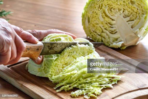 hands of an elderly woman cutting the savoy cabbage with an old knife on a chopping board - chop stock pictures, royalty-free photos & images