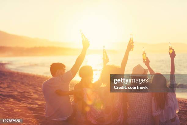 gruppe von jungen leuten, die bei sonnenuntergang am strand feiern. - drinking beer festival stock-fotos und bilder