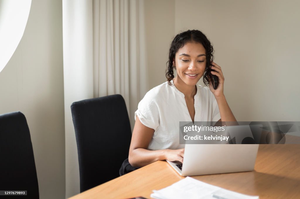 Giovane donna felice che parla al telefono e usa un laptop in un ufficio