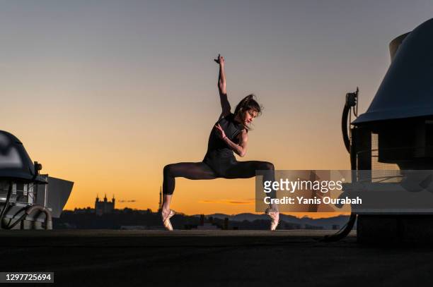 female ballet dancer dancing on a rooftop at sunset in lyon with pointes shoes and bodysuit - woman stretching sunset stock-fotos und bilder
