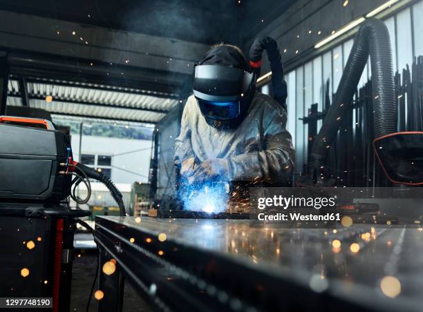 metal worker wearing protective workwear welding metal while working at factory - industrial laborer foto e immagini stock