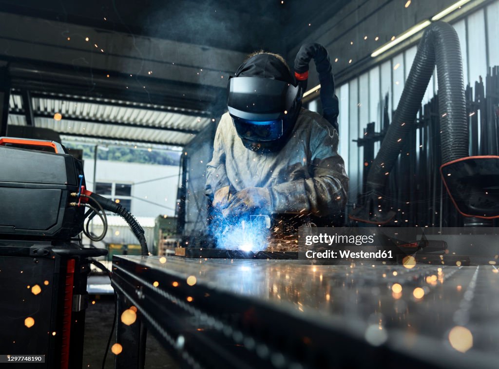 Metal worker wearing protective workwear welding metal while working at factory
