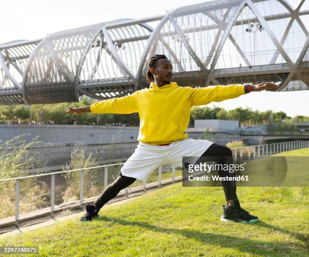 male athlete practicing warrior pose while exercising against walkway - warrior position stock pictures, royalty-free photos & images