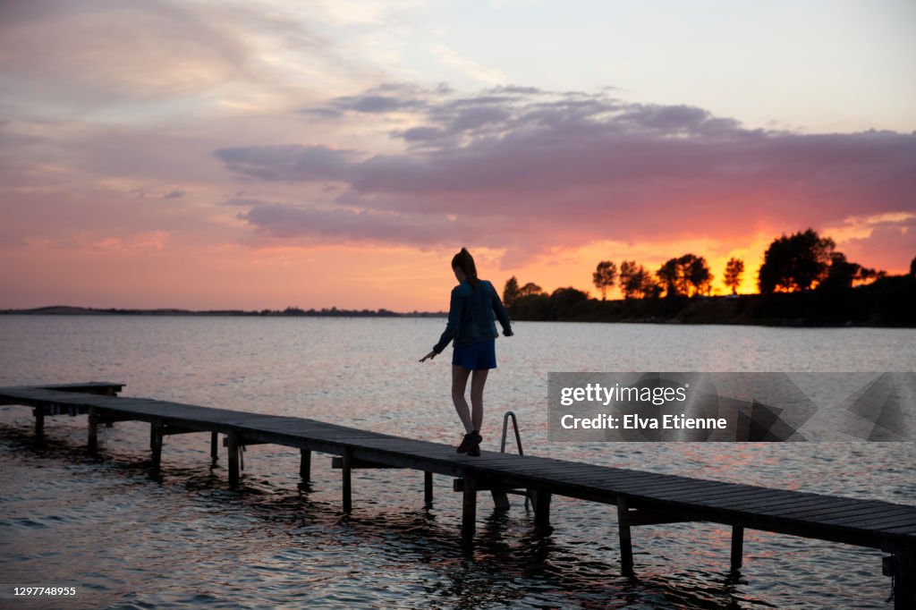Teenage girl balancing carefully along a jetty in the Baltic Sea at sunset