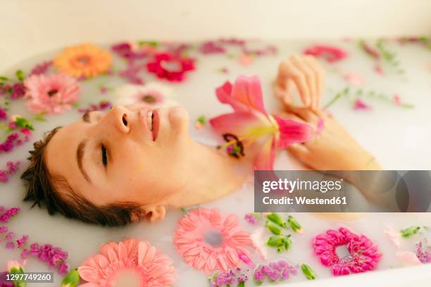 young woman amidst flowers taking milkbath in bathtub at spa - milchbad stock-fotos und bilder