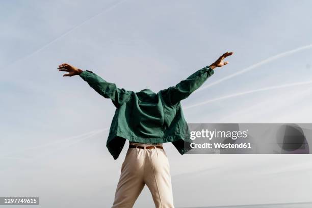 young man with arms outstretched dancing against sky - veste homme photos et images de collection