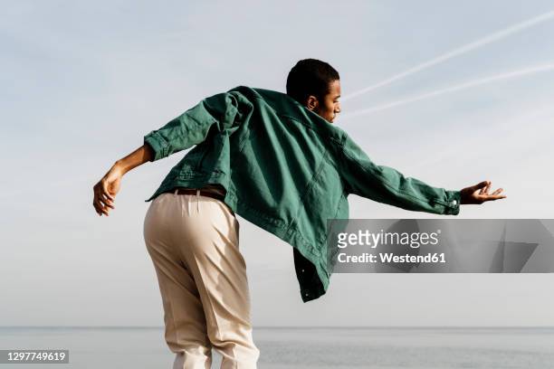 carefree man dancing against sea and sky - green coat 個照片及圖片檔
