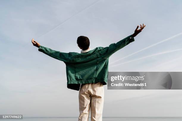 young man with arms outstretched against sky - man in denim jacket stock pictures, royalty-free photos & images