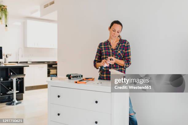woman changing drill bit while standing by cabinet at home - drill bit stockfoto's en -beelden