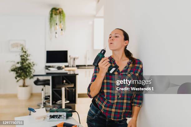 woman holding electric drill while leaning on wall at home - holding tool stock pictures, royalty-free photos & images