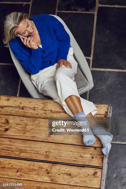 mature woman with gray hair talking on smart phone while leaning leg on table at home - legs in stockings stock pictures, royalty-free photos & images