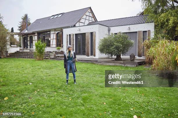 mature woman with hands in pockets standing on grass against built structure - grey hair cool woman stock-fotos und bilder