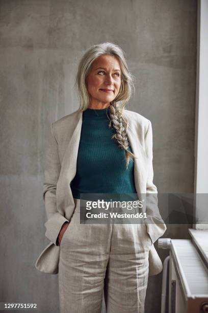 smiling businesswoman with cool attitude looking away against gray wall - grey blazer stock-fotos und bilder