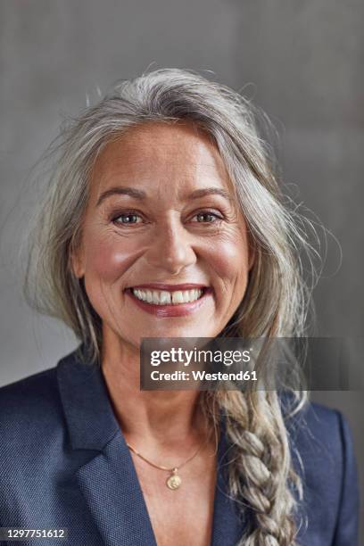 happy businesswoman with gray hair against wall at home office - hair woman mature grey hair beauty stockfoto's en -beelden