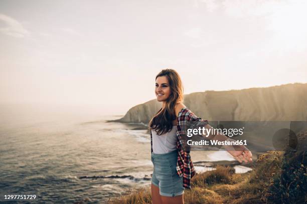 smiling woman with arms outstretched looking at view while standing against sky - arms outstretched fotografías e imágenes de stock