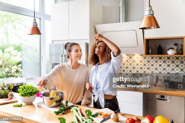 businesswoman with colleague tasting spaghetti in office kitchen - kochen stock-fotos und bilder