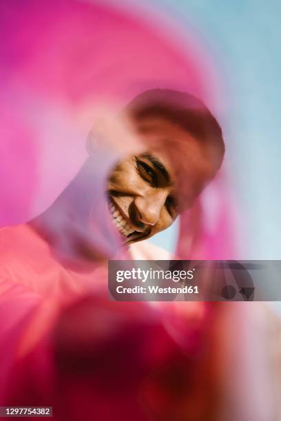smiling man looking through rolled up plastic against sky - clear sky stockfoto's en -beelden