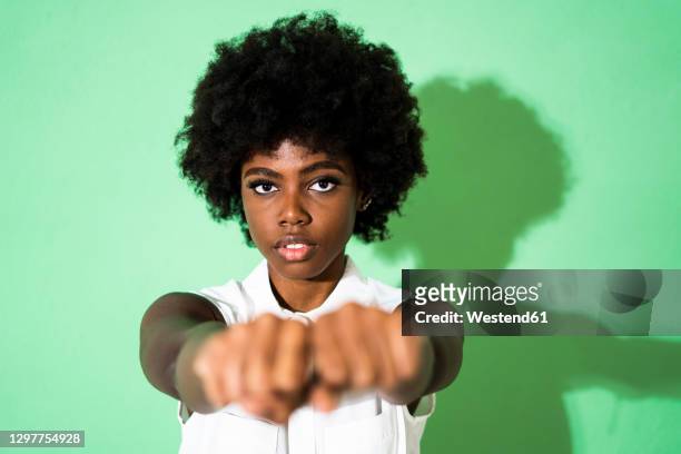 young woman showing fist while standing against green background - strong hair 個照片及圖片檔