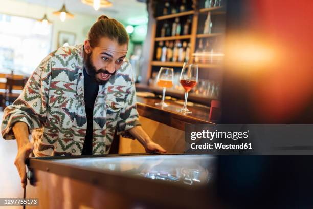 cheerful bearded man playing pinball in bar - flipper stock-fotos und bilder