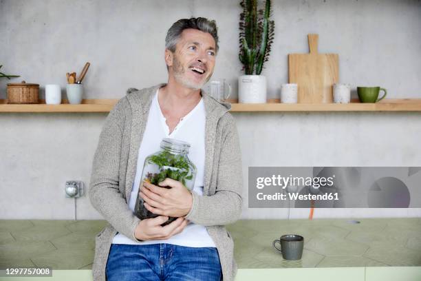 mature man smiling while holding terrarium sitting at home - terrarium stock pictures, royalty-free photos & images