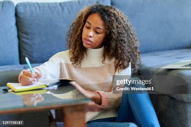 afro young woman with laptop writing in notepad at home - diary photos et images de collection