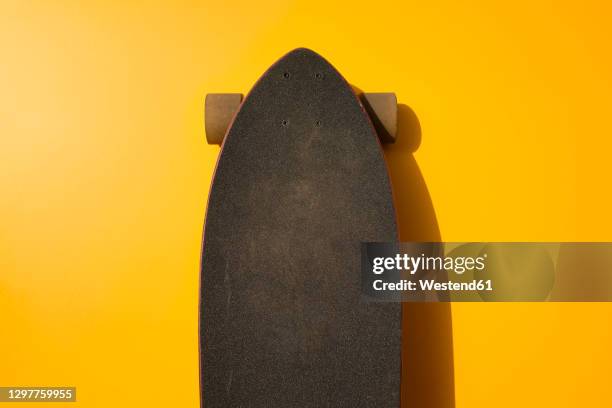 black longboard leaning on yellow wall - skateboard stock pictures, royalty-free photos & images