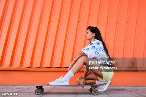 portrait of beautiful girl crouching beside longboard in front of corrugated iron wall - short hair photos et images de collection