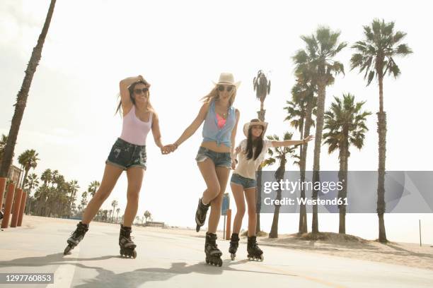 happy female friends roller skating by beach against clear sky on weekend - patín en línea fotografías e imágenes de stock