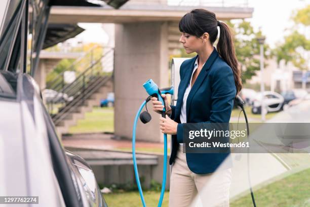 businesswoman holding electric car charger at station - electric car charger imagens e fotografias de stock