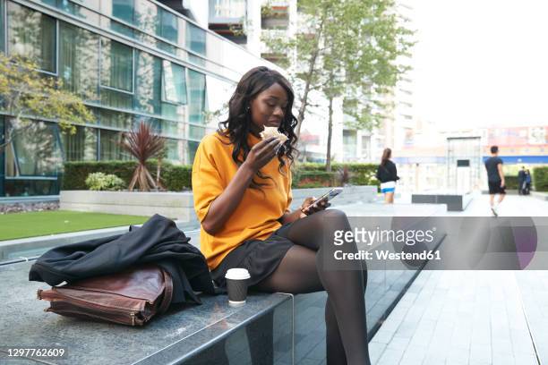 businesswoman having sandwich while using mobile phone at office park - business park uk fotografías e imágenes de stock