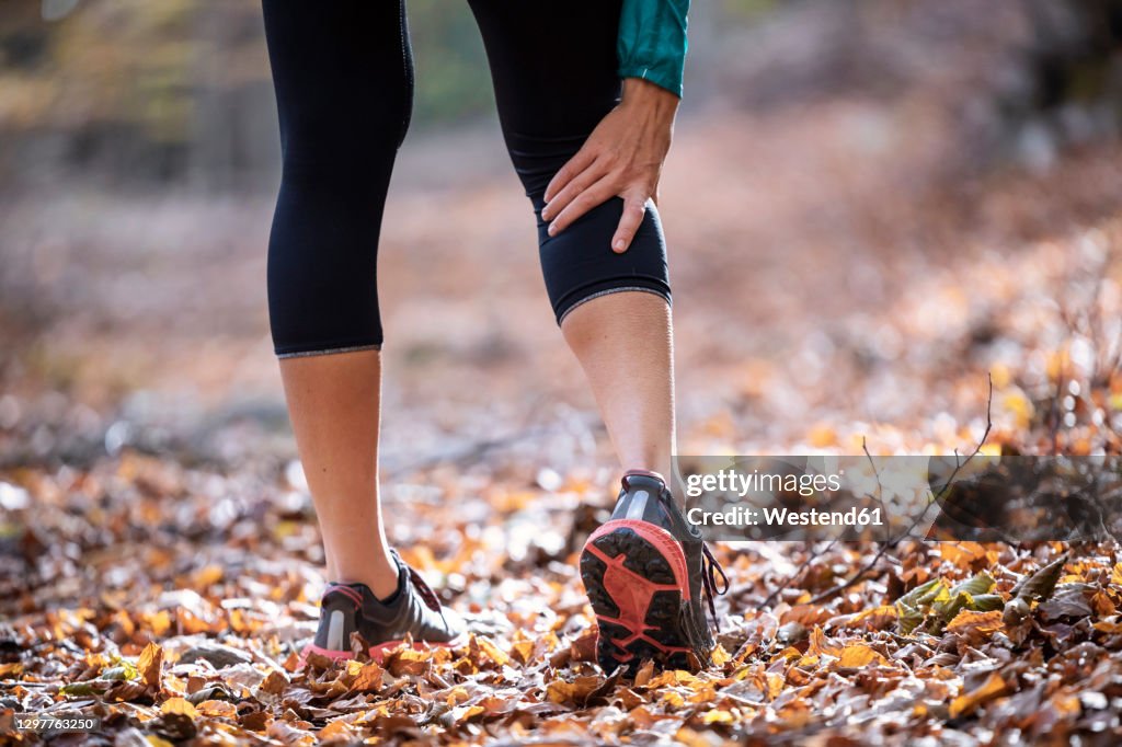 Sportswoman having cramp in leg while standing on forest path