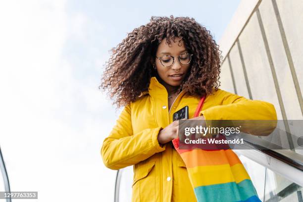 woman searching in purse while standing on escalator against sky - multi colored purse stock pictures, royalty-free photos & images