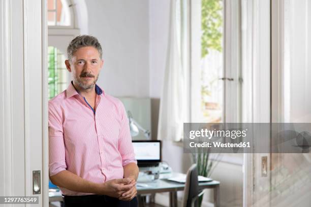 confident businessman leaning on doorway of office - pink collared shirt stock pictures, royalty-free photos & images